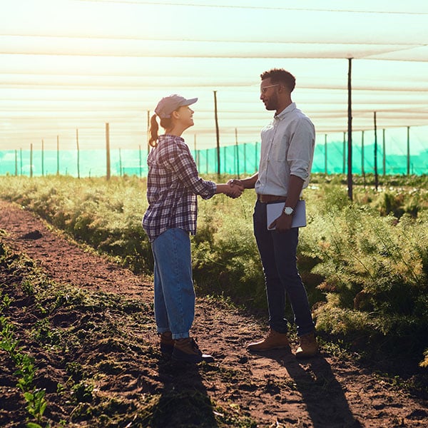 Full length shot of two young farmers shaking hands while working on their farm